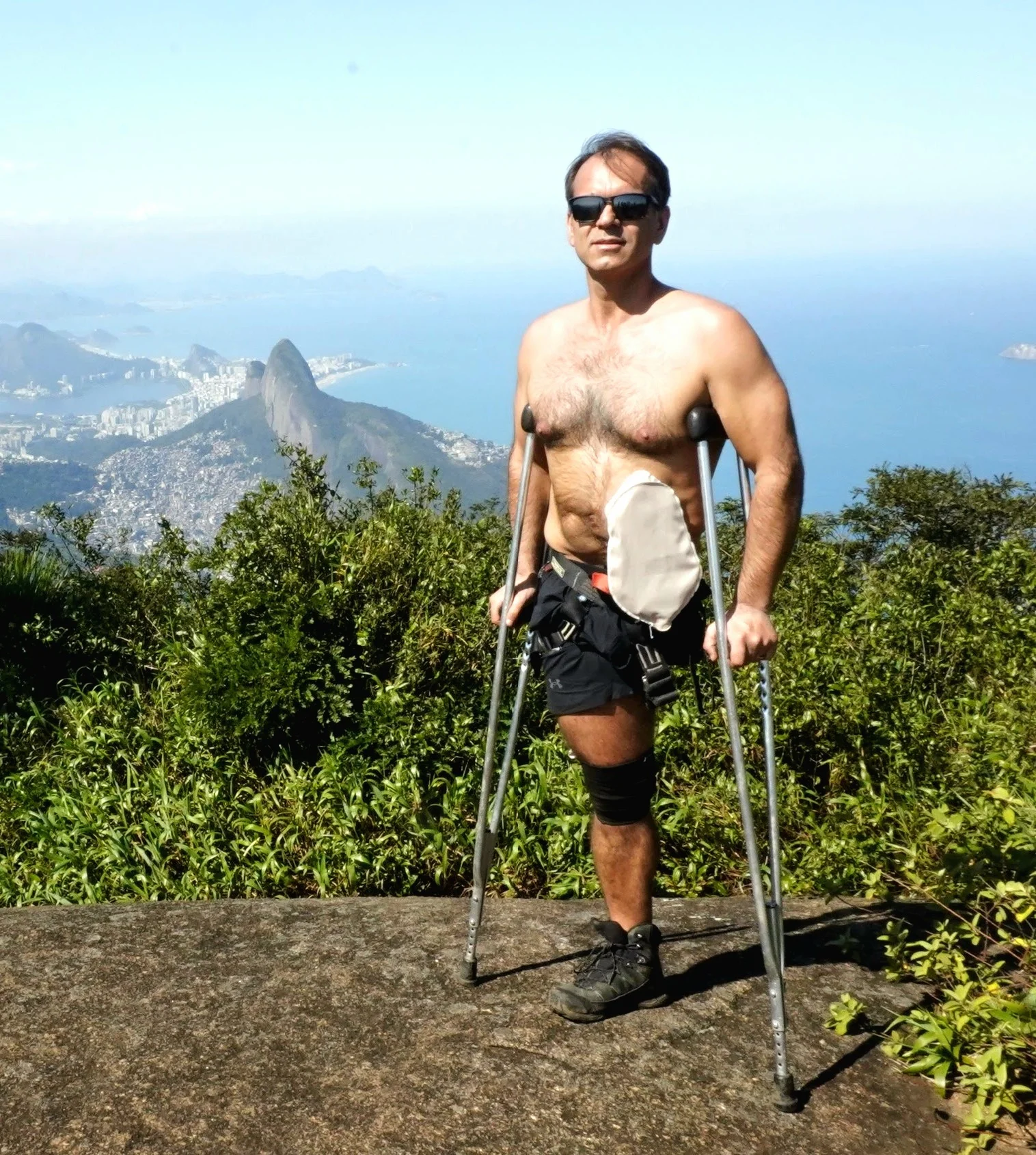 um homem com uma bengala em pé sobre uma rocha com árvores e montanhas ao fundo