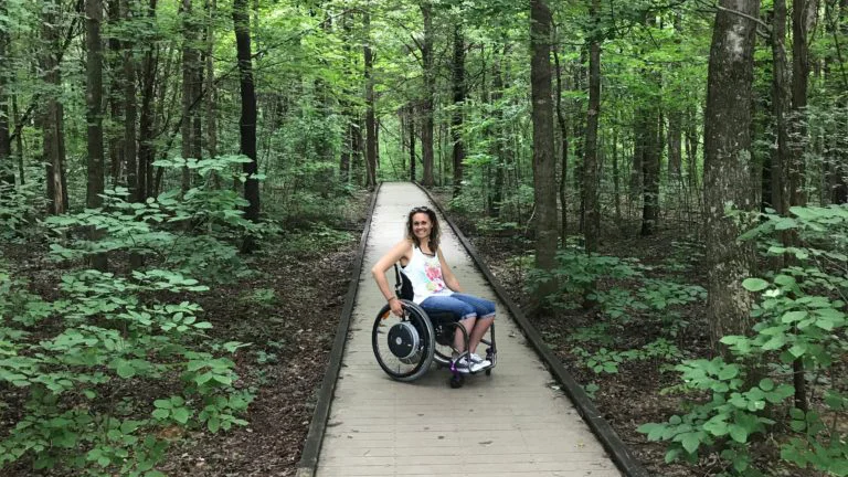 Arlene in a wheelchair on a path in the woods 